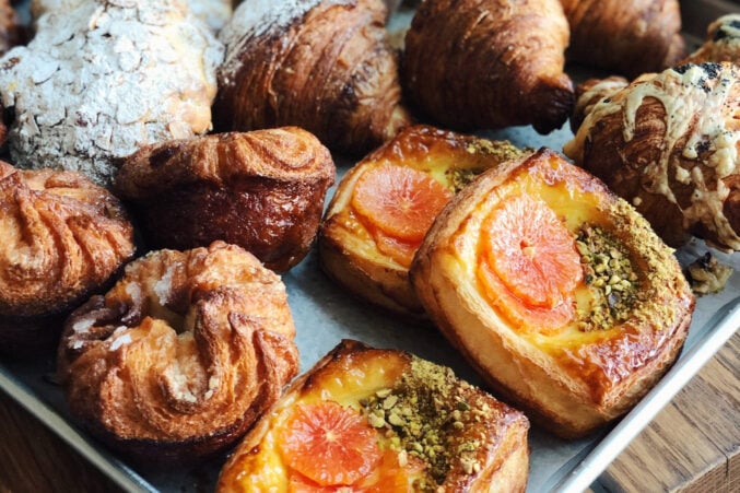 A tray of pastries like croissant, cara cara orange danishes, and kouign ammans.